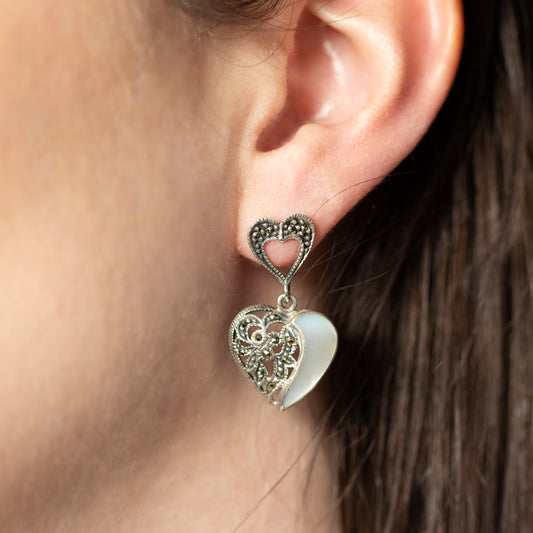 An ear wearing a silver heart shaped filigree drop earring, set with mother of pearl and marcasites