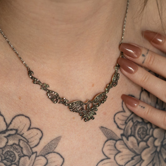 A highly decorative openwork collar necklace, set with marcasites in an Art Deco style, being worn against a tattooed chest.