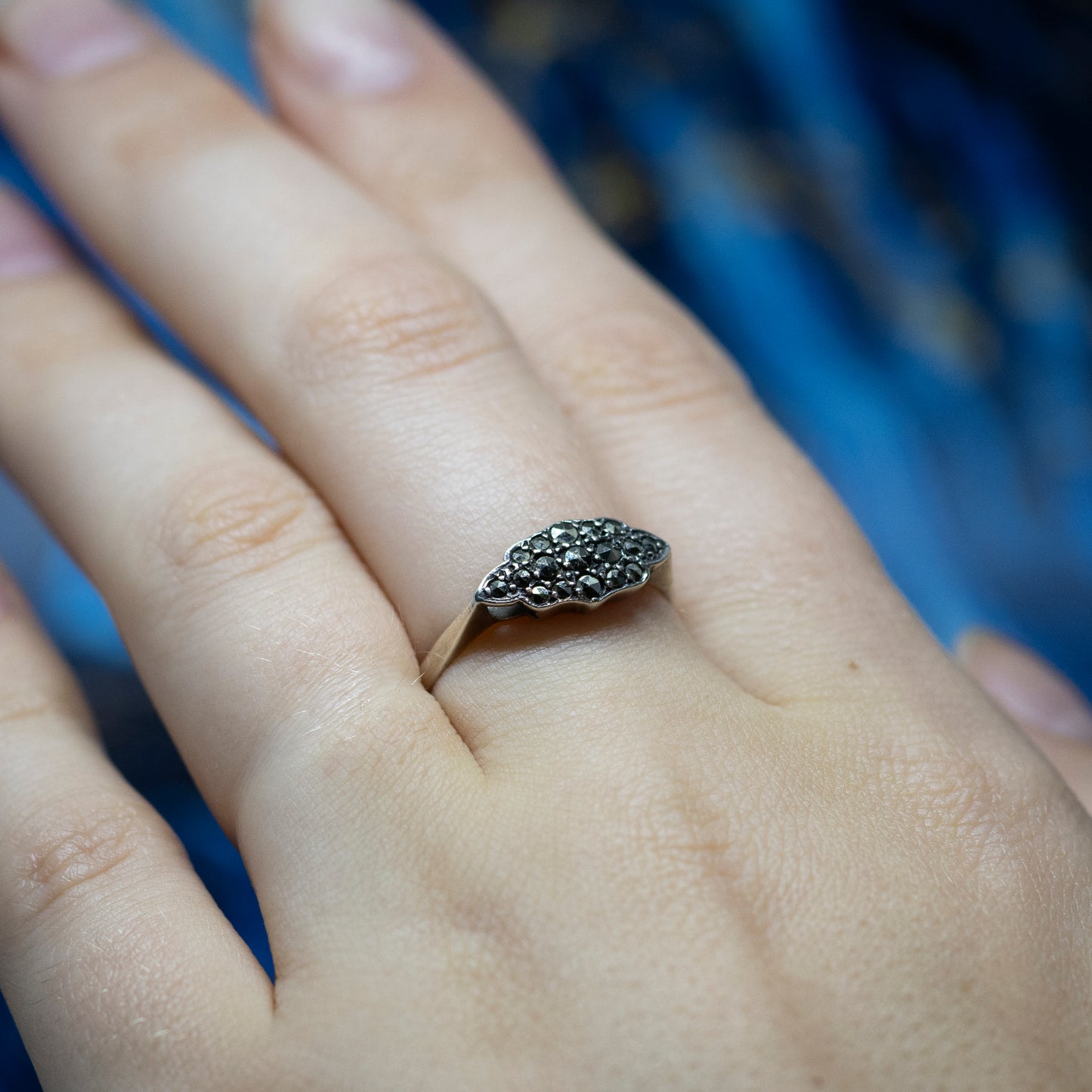 A silver Art Deco style cluster ring set with marcasites, being worn on the middle finger of a hand.