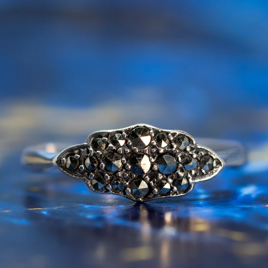 A silver Art Deco style cluster ring set with marcasites, on a blue background.