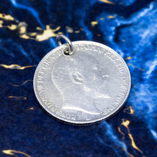 A silver sixpence pendant showing the profile of Edward VII, on a blue and gold marble background.