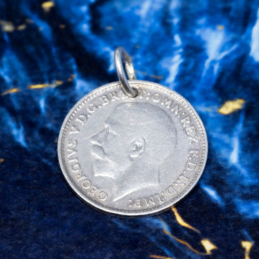 A silver threepence pendant showing the profile of George V, on a blue and gold marble background.