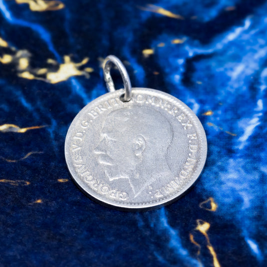 A silver threepence pendant showing the profile of George V, on a blue and gold marble background.