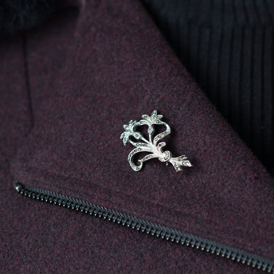 A vintage style silver and marcasite floral design brooch, worn on the collar of a burgundy dress coat.