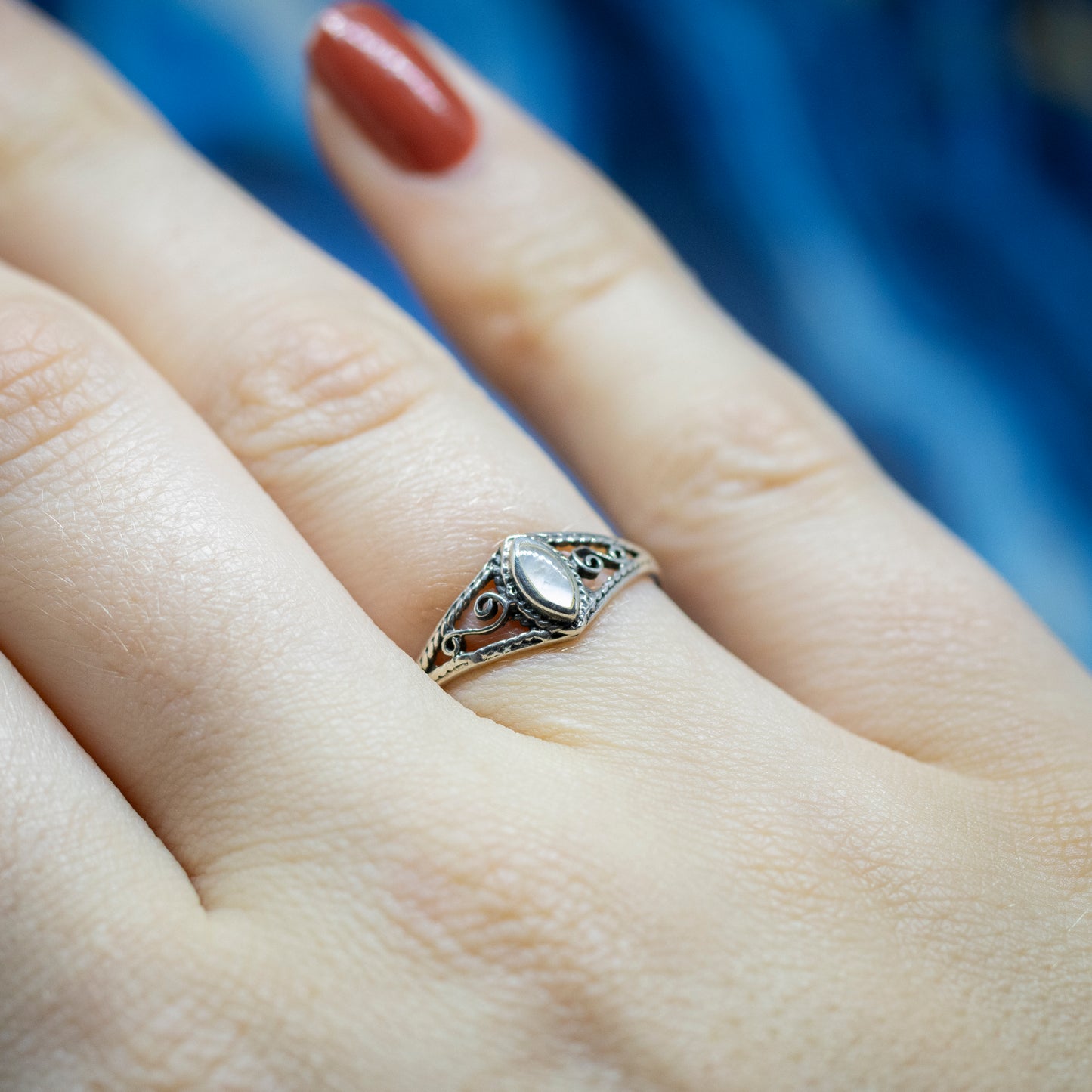 A marquise shape mother of pearl silver ring, with openwork scroll design shoulders, being worn on a hand.