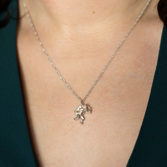 A silver cupid necklace being worn around a neck.