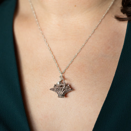 A silver flower basket necklace being worn around a neck.