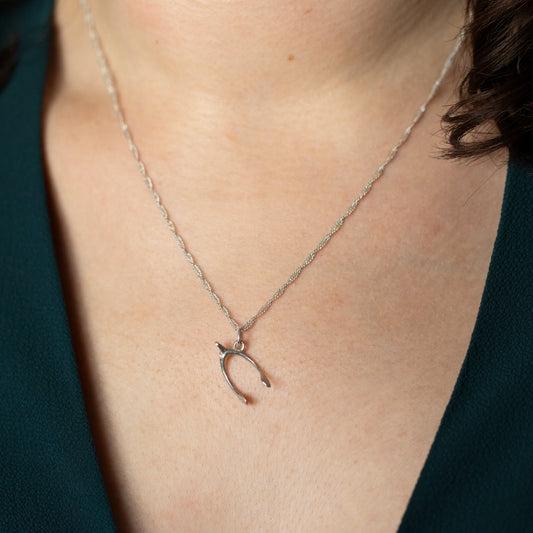 A silver wishbone necklace being worn around a neck.