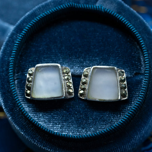 A pair of geometric shaped stud earrings with a large polished stone in the centre of each, and marcasites down either side, in a blue box.