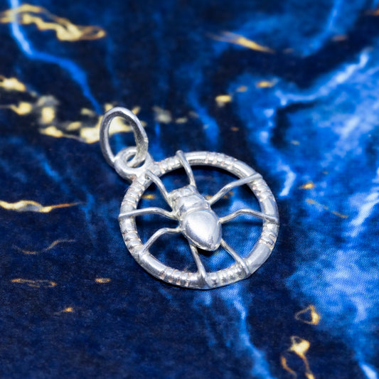 A silver openwork spider pendant on a blue and gold marble background.