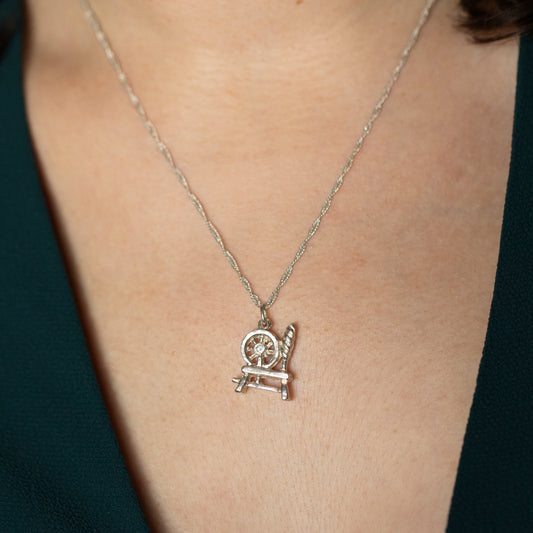 A silver spinning wheel necklace being worn around a neck.