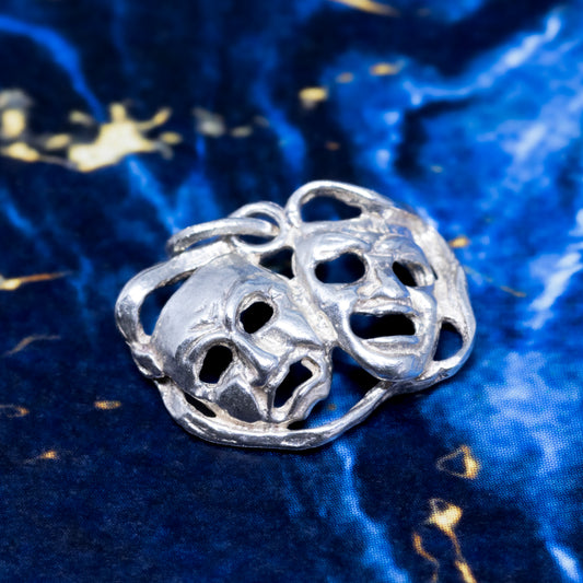 A silver theatre masks pendant, on a blue background.