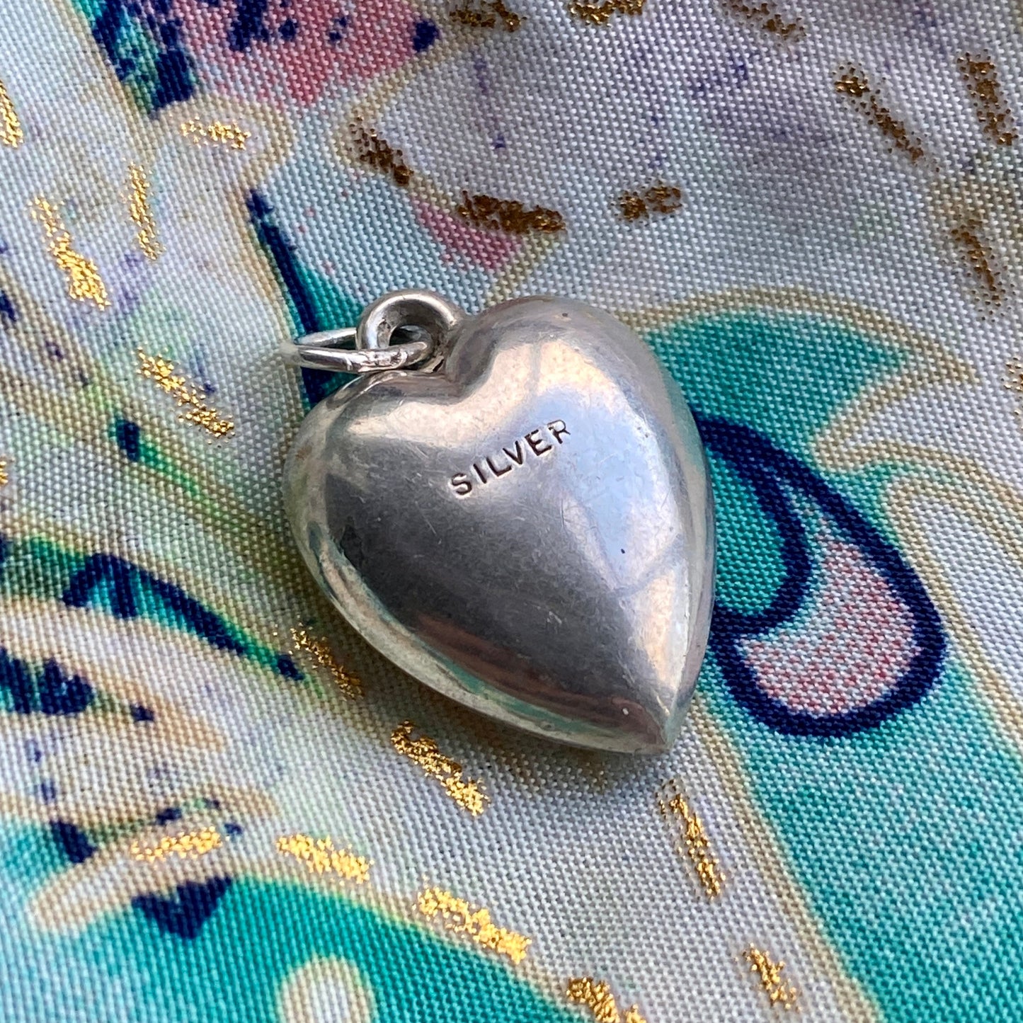 Silver heart-shaped pendant on a colorful fabric background