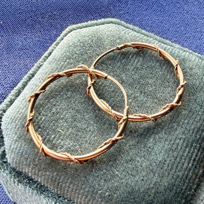 Rose gold hoop earrings on a textured surface with a blue background