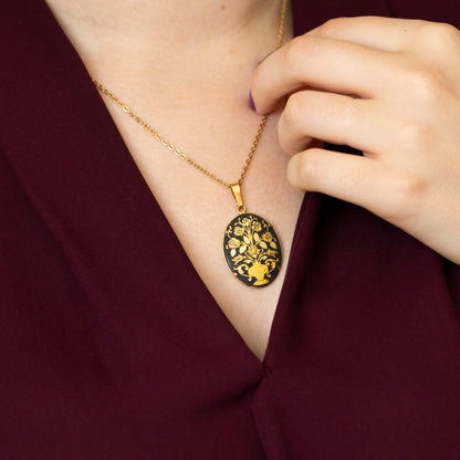 An oval black and gold-coloured damascene pendant on a chain, being worn around a neck with a red blouse.