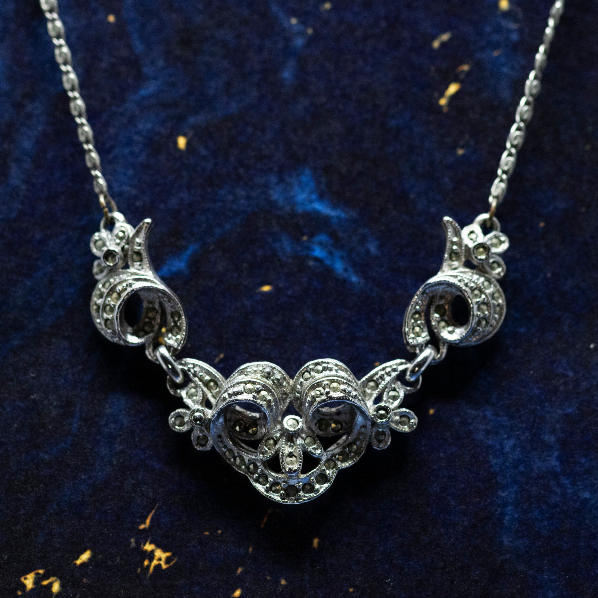 A vintage style silver and marcasite collar necklace, on a blue background.