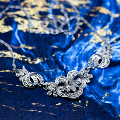A vintage style silver and marcasite collar necklace, on a blue and gold marble background.