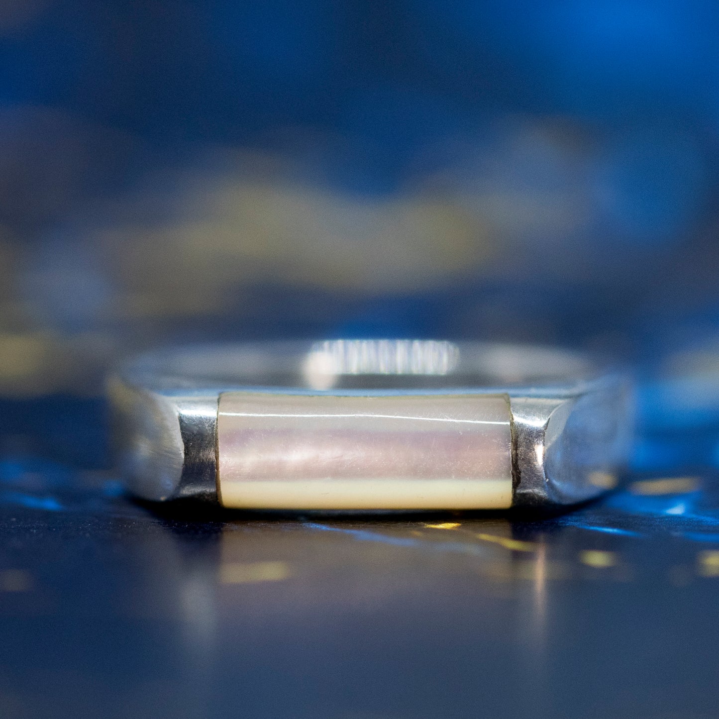 A silver mother of pearl bar ring, on a blue and gold marble surface.