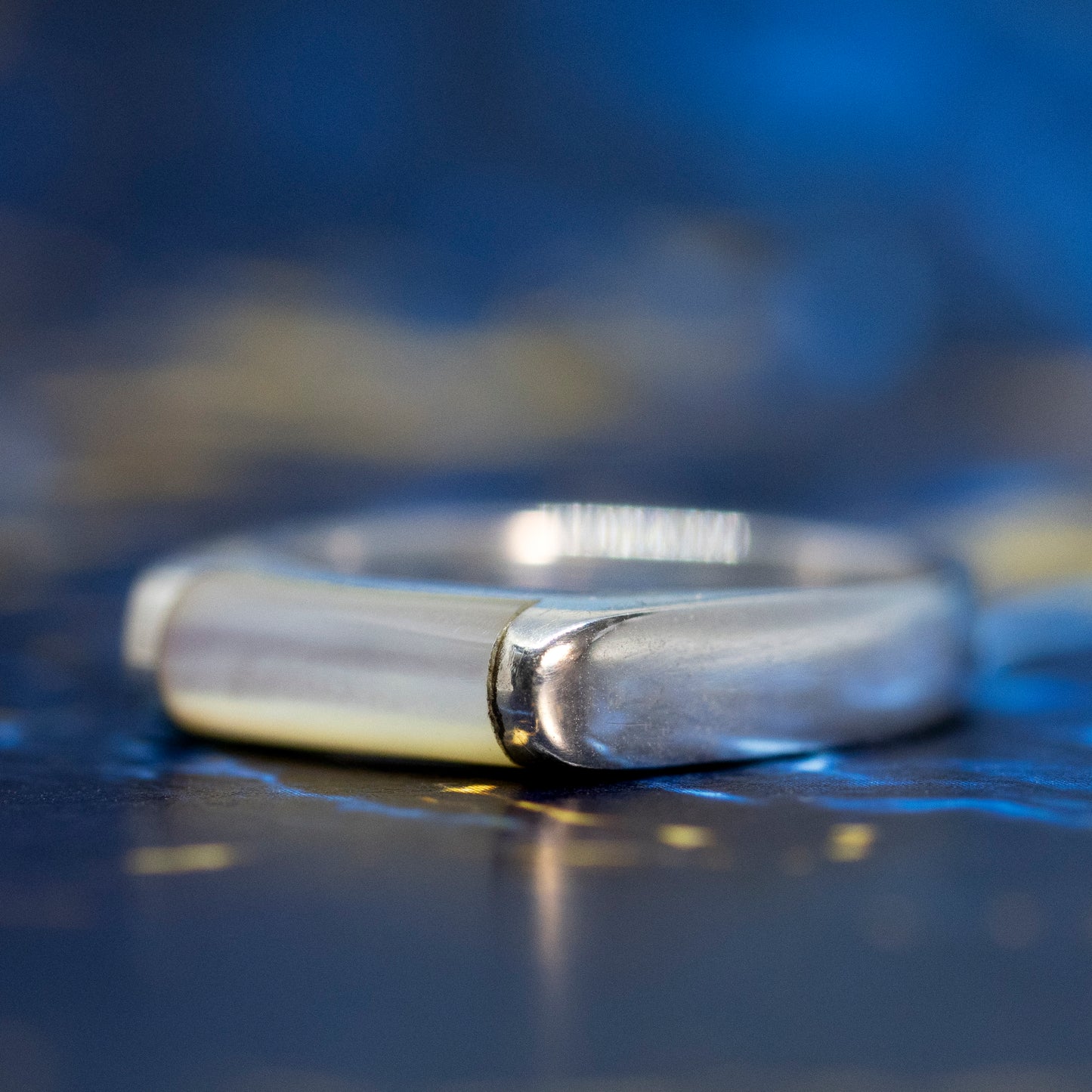 The side profile of a silver mother of pearl bar ring, on a blue and gold marble surface.