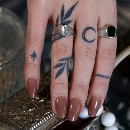 A tattooed hand, wearing a silver textured heart shape signet ring and a silver onyx signet ring, opening a vintage jewellery box.
