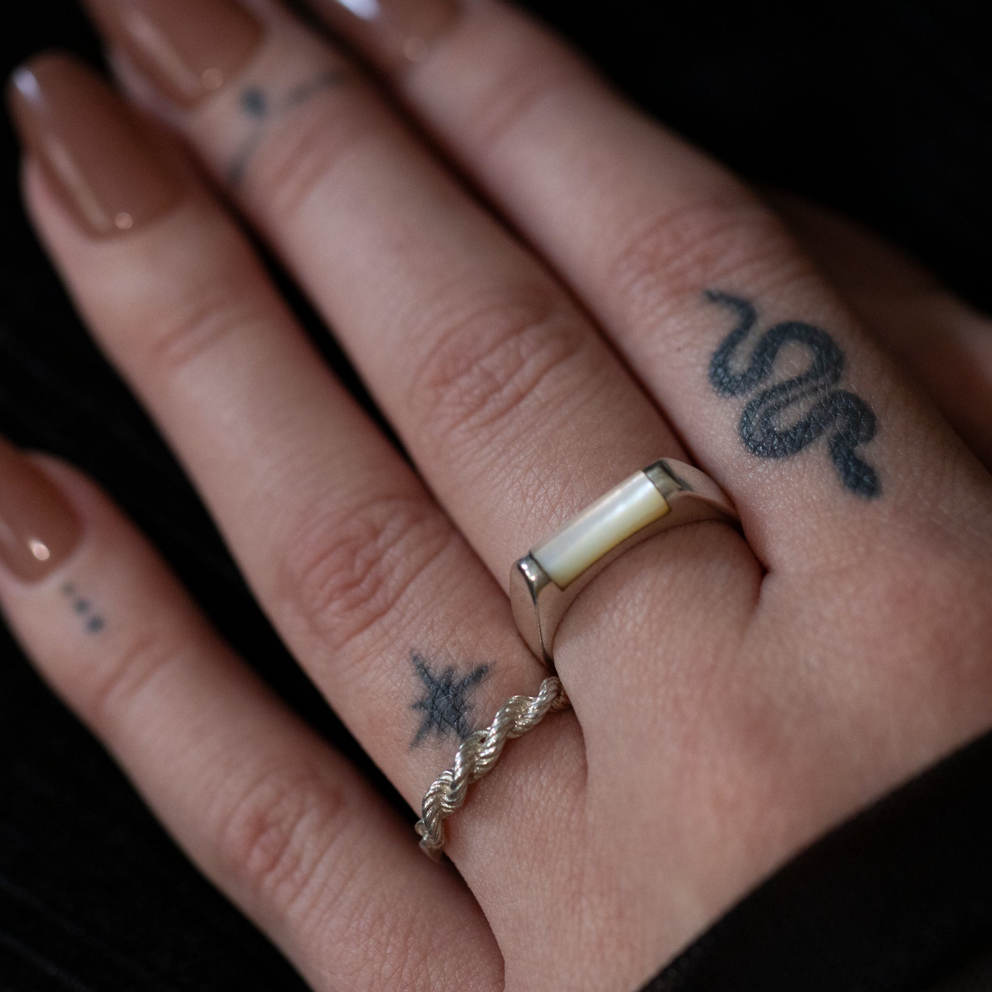 A tattooed hand wearing a silver mother of pearl bar ring and a silver twisted rope design ring.