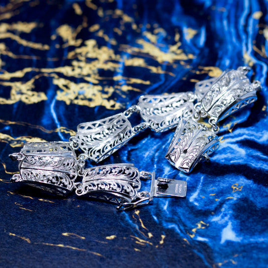 An  intricate filigree design silver panel bracelet, with a blue background.