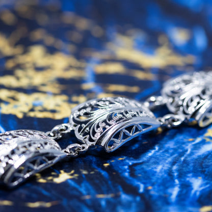 A close-up of an intricate filigree design silver panel bracelet, with a blue and gold marble background.