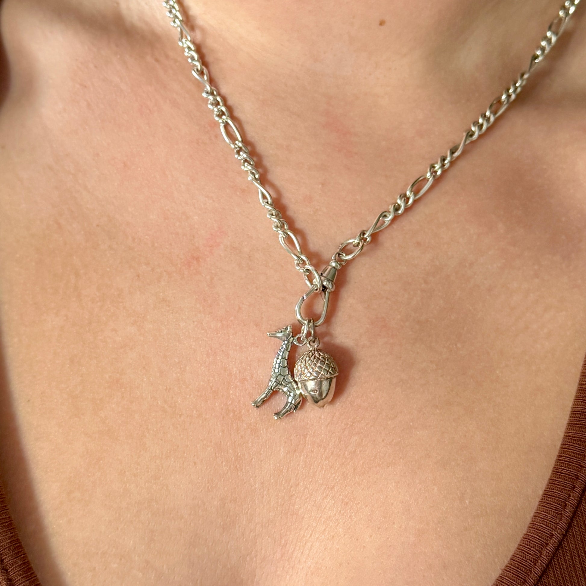 Silver necklace with a giraffe and an acorn pendant on a person's neck.