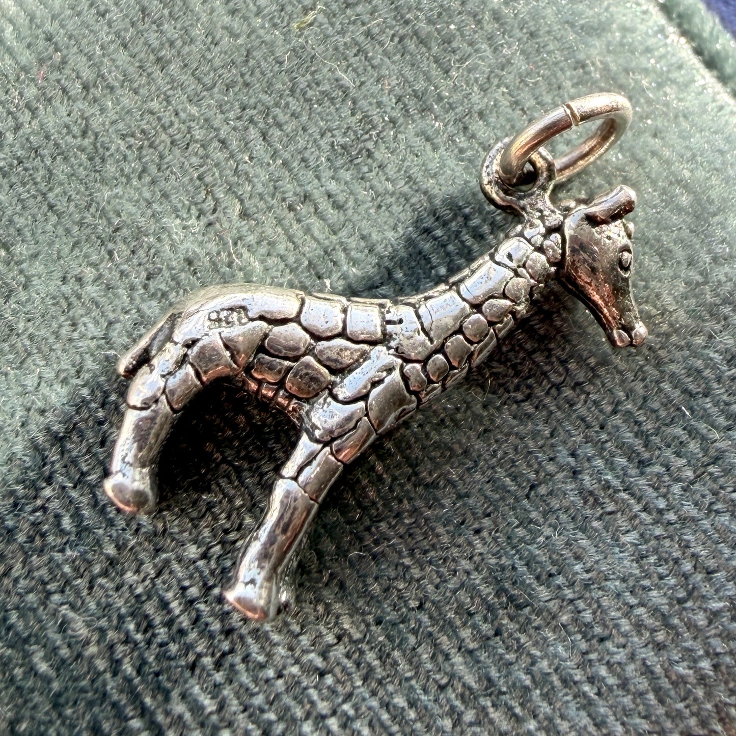 Silver giraffe pendant on a textured green background