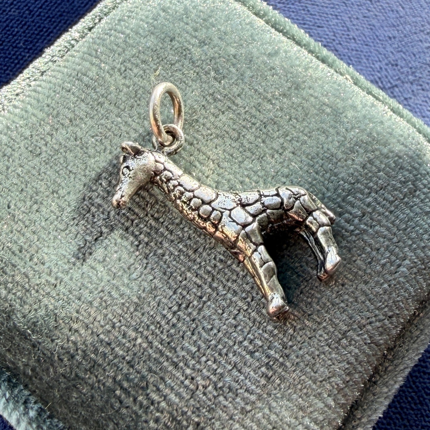 Silver giraffe pendant on a green velvet cushion