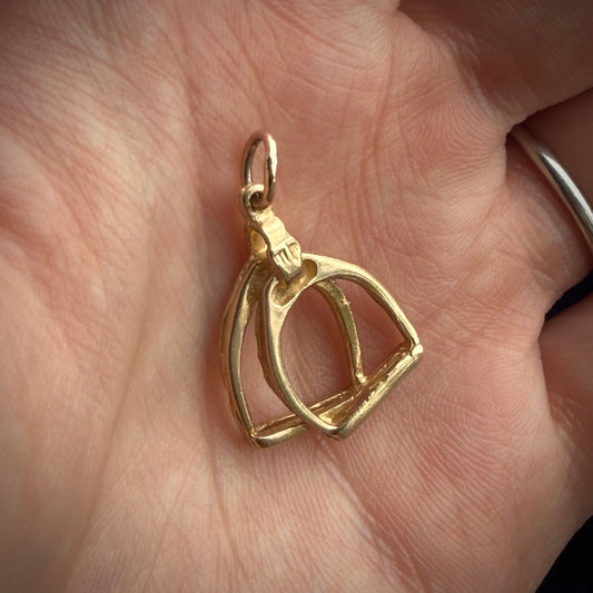 A gold stirrups pendant on a hand.