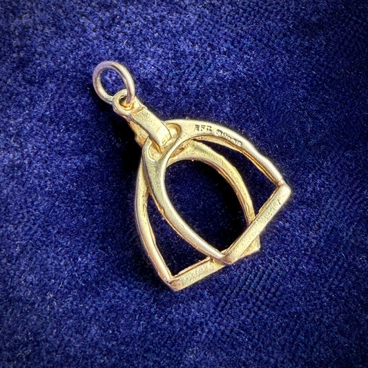 A gold stirrups pendant with 9ct hallmark on a blue velvet background.