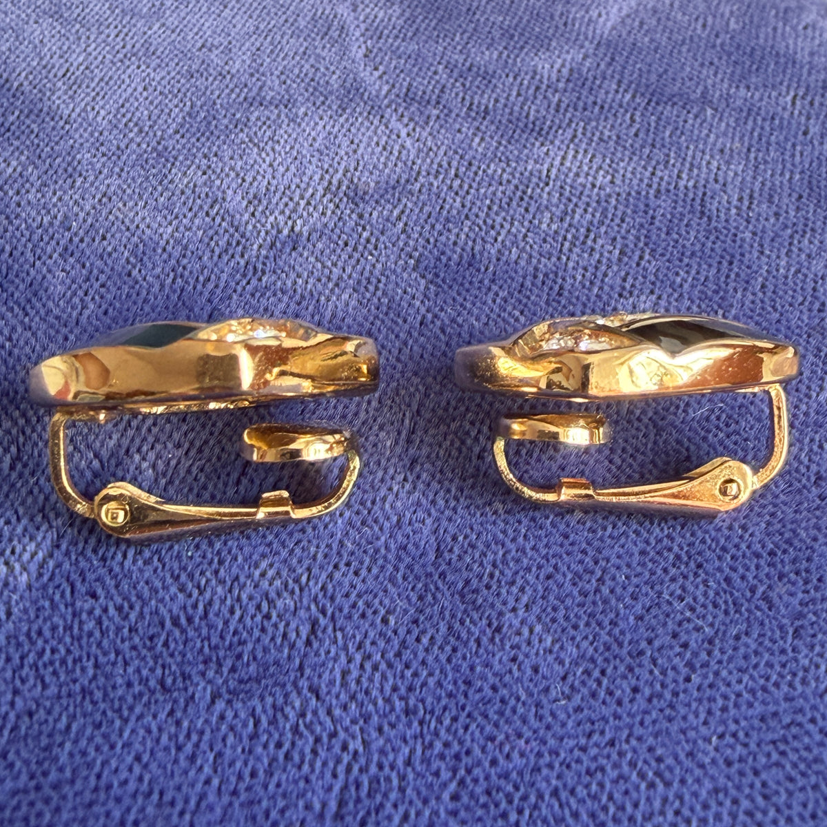 Side view of a pair of gold-tone clip-on earrings, displayed on a textured blue fabric background.