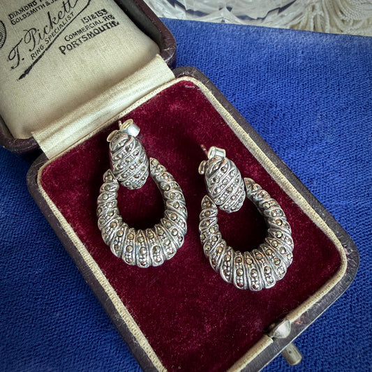 A pair of vintage silver and marcasite hinged drop earrings with intricate twist detailing, presented in an open vintage box with a red velvet lining. 
