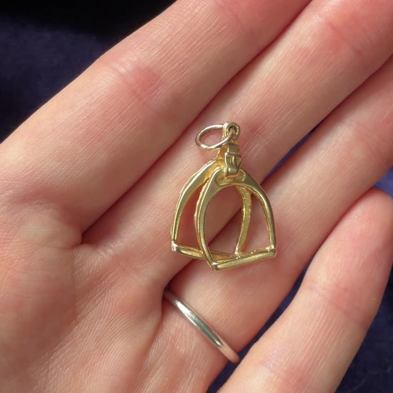 A video of a vintage gold stirrup charm pendant on a hand.